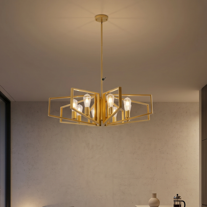 Gold chandelier hanging in a room with a neutral wall and a small table with a vase and coffee press.